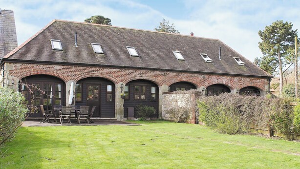 A brick building with a sloped roof and multiple windows. There is a lawn in front with a table and chairs. - 2 bedroom accommodation in Apse Wood, near Shanklin (Apse Wood, near Shanklin)