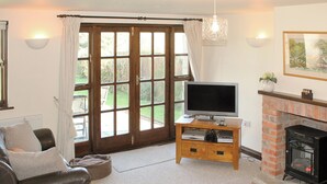 A living room with a leather sofa, a TV on a wooden stand, a fireplace, and a large window with curtains. - 2 bedroom accommodation in Apse Wood, near Shanklin (Apse Wood, near Shanklin)