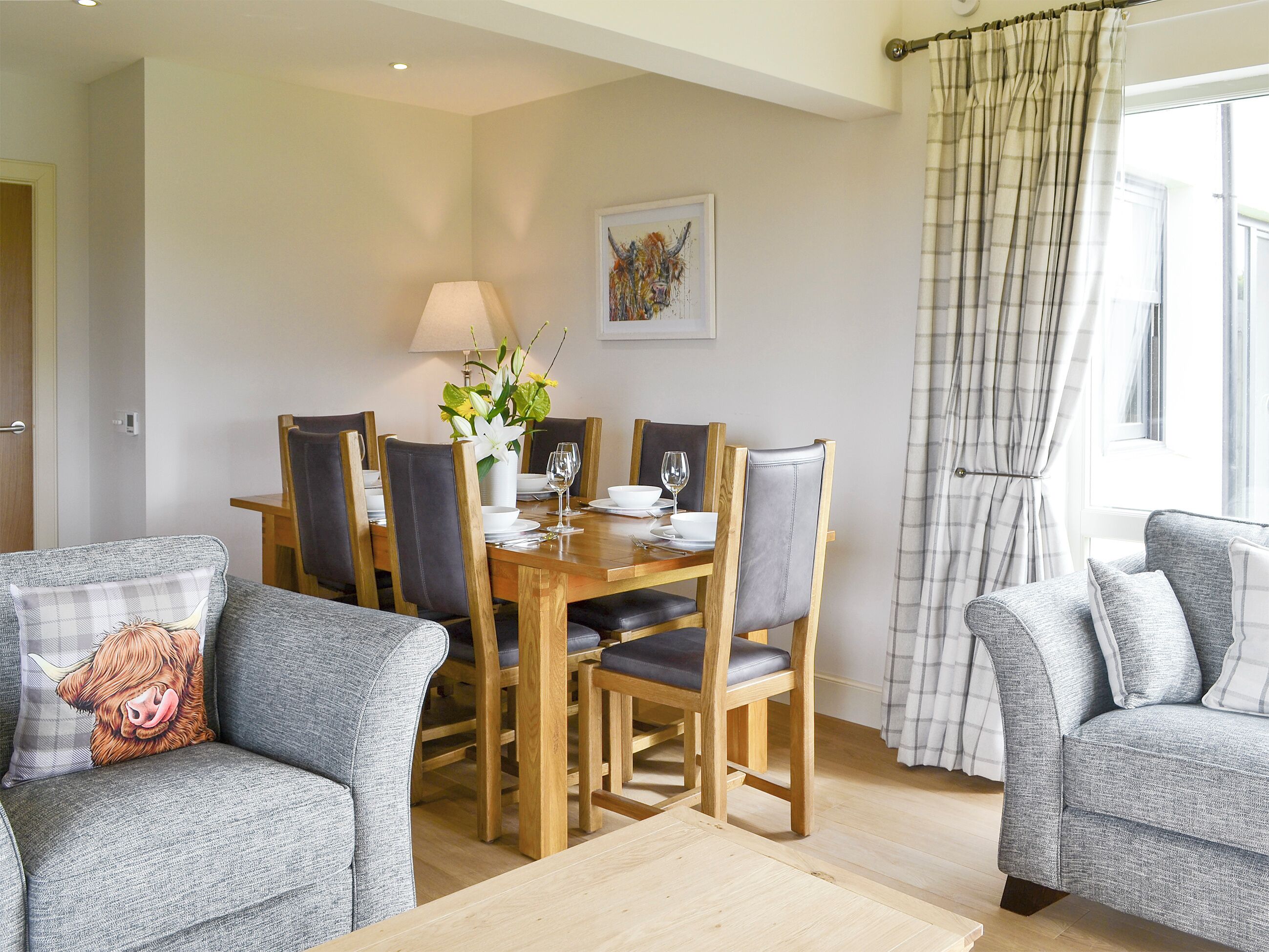 A dining area with a wooden table, chairs, a vase with flowers, and a painting on the wall.