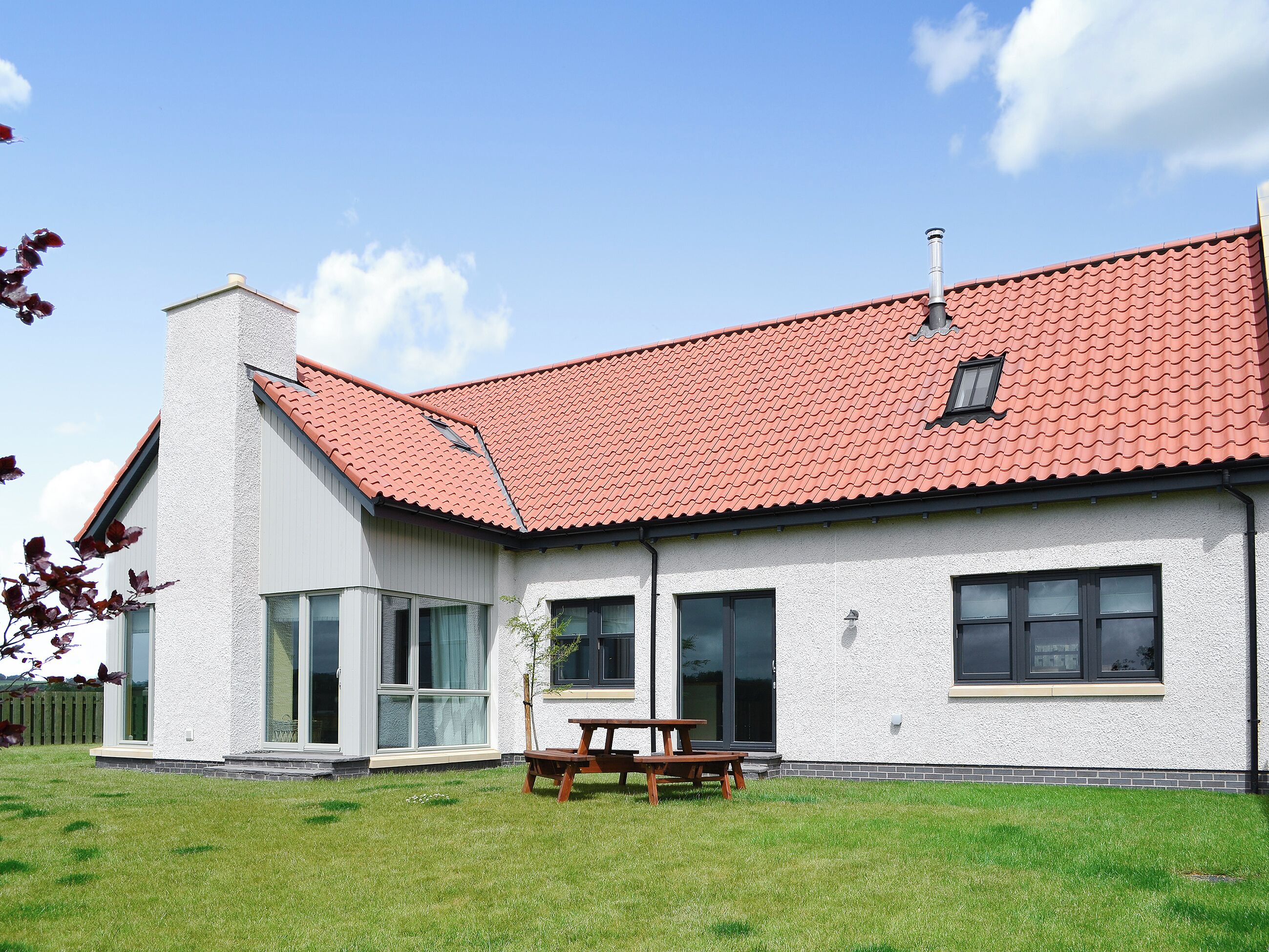 A single-story house with a red-tiled roof, large windows, and a visible chimney.