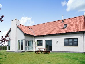 A single-story house with a red-tiled roof, large windows, and a visible chimney.