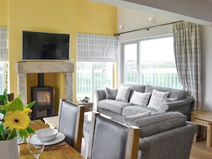 A living room with a fireplace, a sofa set, a dining table with chairs, and a TV mounted on the wall.