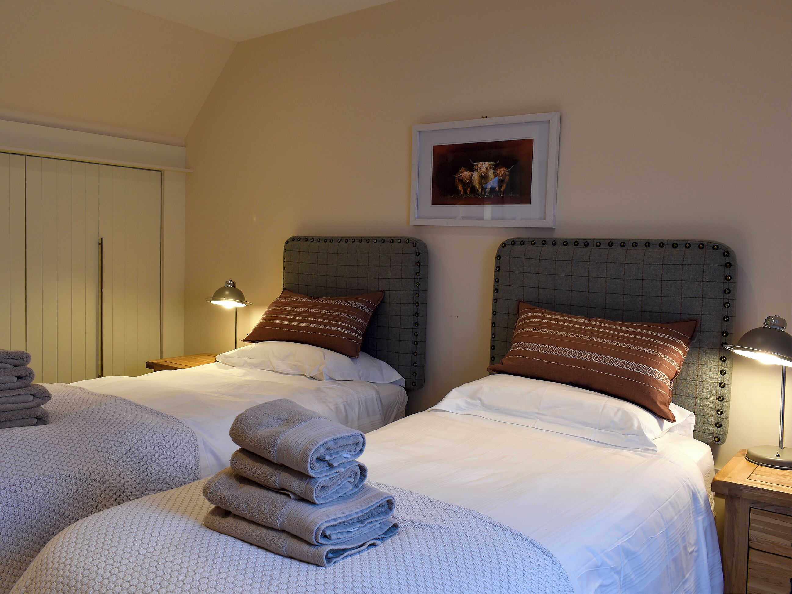 Ein Hotelzimmer mit zwei Betten, jeweils mit Kopfteil, Kissen und gefalteten Handtüchern. Darüber an der Wand hängt ein gerahmtes Bild.