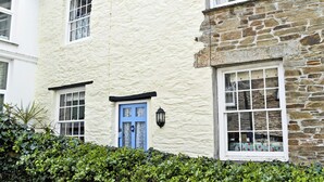 A two-story building with a white exterior and a stone facade. There are multiple windows with white frames and a blue door. - 3 bedroom accommodation in Polruan-by-Fowey (Polruan-by-Fowey)