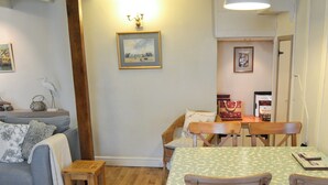A cozy living room with a sofa, a small wooden table, and a dining table with chairs. There is a framed painting on the wall and a lamp on the table. - 3 bedroom accommodation in Polruan-by-Fowey (Polruan-by-Fowey)