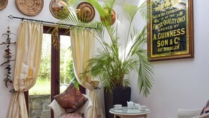 Une pièce chaleureuse avec un fauteuil en osier, une petite table avec des tasses, une plante en pot et un panneau décoratif encadré.