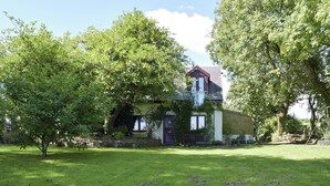 Une maison avec un toit en pente, entourée d’arbres verdoyants et d’une pelouse bien entretenue.
