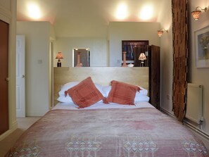 A bedroom with a large bed, two bedside lamps, a mirror above the bed, and a door on the left.