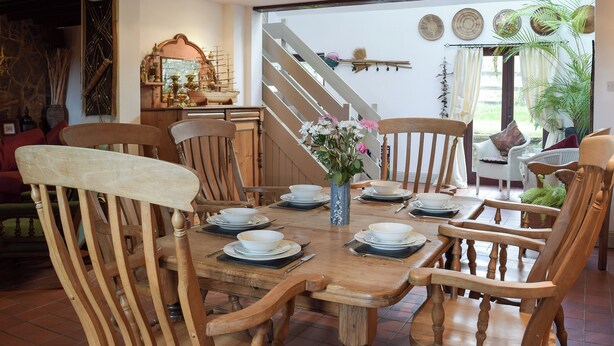 Un coin repas avec des chaises en bois et une table dressée pour quatre personnes, un escalier menant à l’étage supérieur et une vue sur l’extérieur grâce à une porte vitrée.