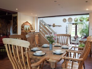 A dining area with wooden chairs and a table set for four, a staircase leading to an upper level, and a view of the outdoors through a glass door.
