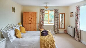 A bedroom with a bed, a wooden wardrobe, a chair, a radiator, and a window with curtains. - 2 bedroom accommodation in Arthog, near Dolgellau (Arthog, near Dolgellau)