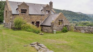A stone house with a sloped roof, a chimney, and a stone wall in the foreground. - 2 bedroom accommodation in Arthog, near Dolgellau (Arthog, near Dolgellau)