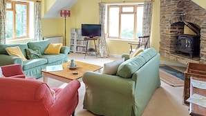 A cozy living room with a stone fireplace, green sofas, a red armchair, and a bookshelf. - 2 bedroom accommodation in Arthog, near Dolgellau (Arthog, near Dolgellau)