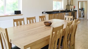 Une cuisine spacieuse avec un coin repas, comprenant une table et des chaises en bois, un plan de travail noir et une vue sur l’extérieur.