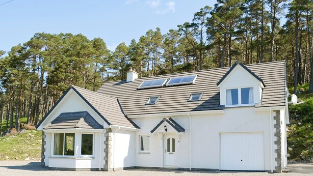Une maison à deux étages avec un toit en pente, un garage et une allée gravillonnée.