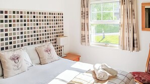 Ett sovrum med en stor säng, en sänggavel med ett mosaikmönster, ett fönster med gardiner och utsikt över ett grönskande landskap.