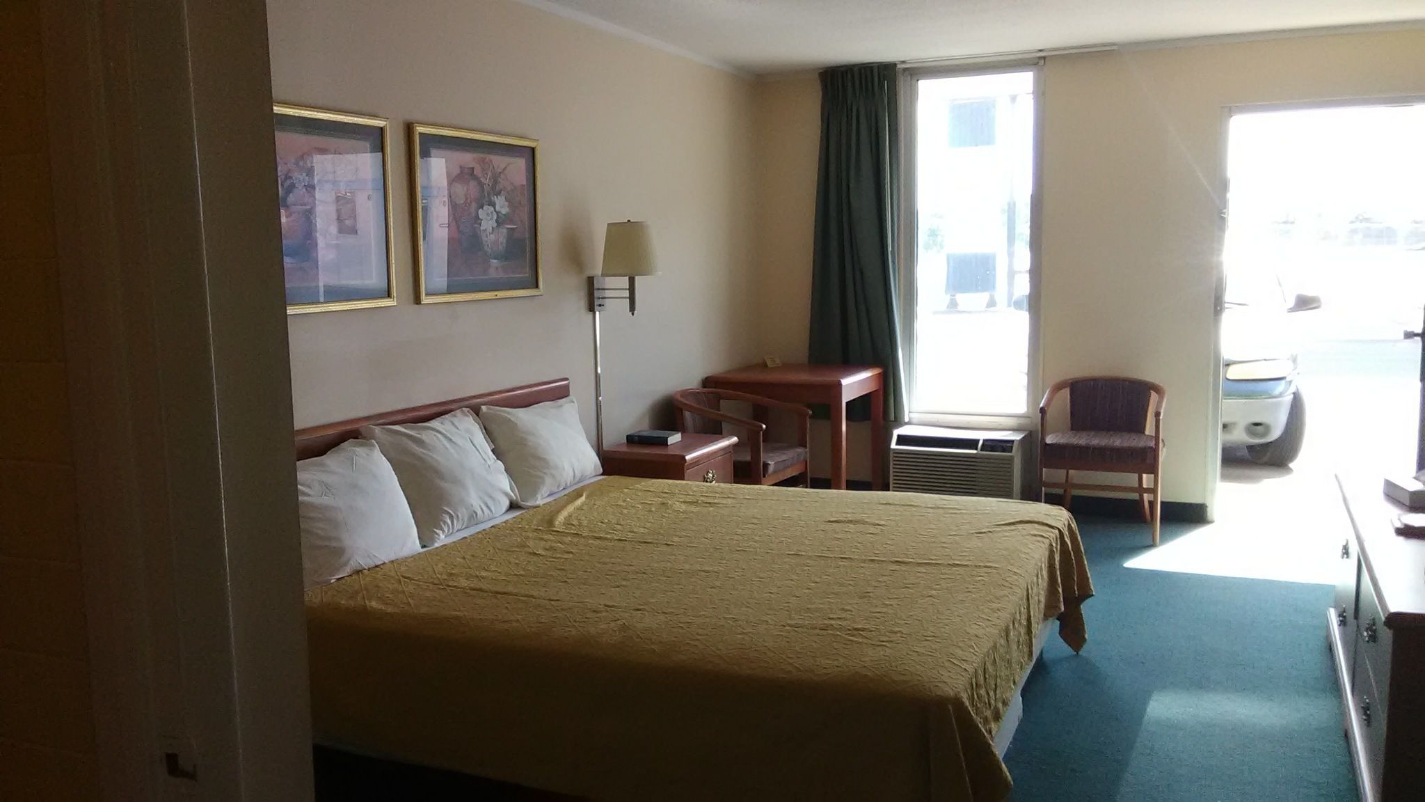Habitación de hotel con cama, escritorio, silla, lámpara y dos cuadros en la pared.