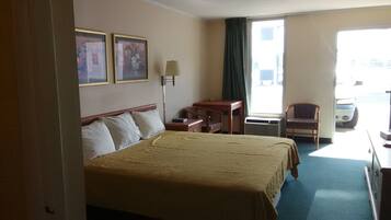 Habitación de hotel con cama, escritorio, silla, lámpara y dos cuadros en la pared.
