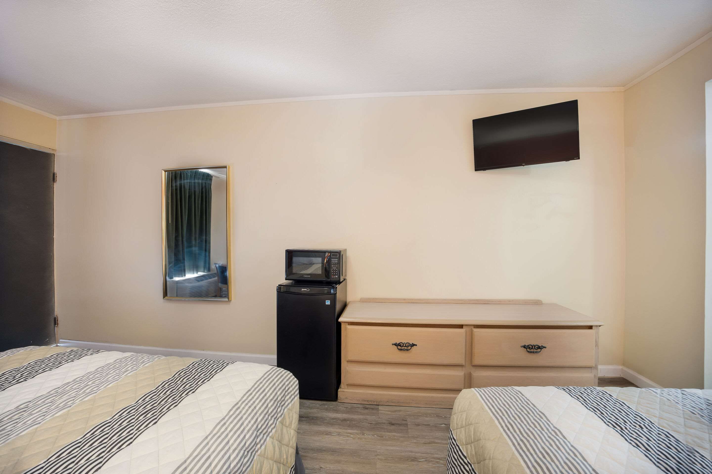 A hotel room with two beds, a small desk with drawers, a microwave, and a flat-screen TV mounted on the wall.