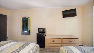 A hotel room with two beds, a small desk with drawers, a microwave, and a flat-screen TV mounted on the wall.