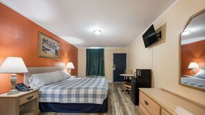 Une chambre d’hôtel avec un lit, des lampes de chevet, un bureau avec un ordinateur, un téléviseur fixé au mur et une porte avec un rideau vert.
