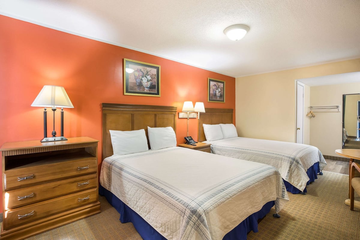 A hotel room with two beds, a wooden dresser, a desk with a lamp, and a mirror.