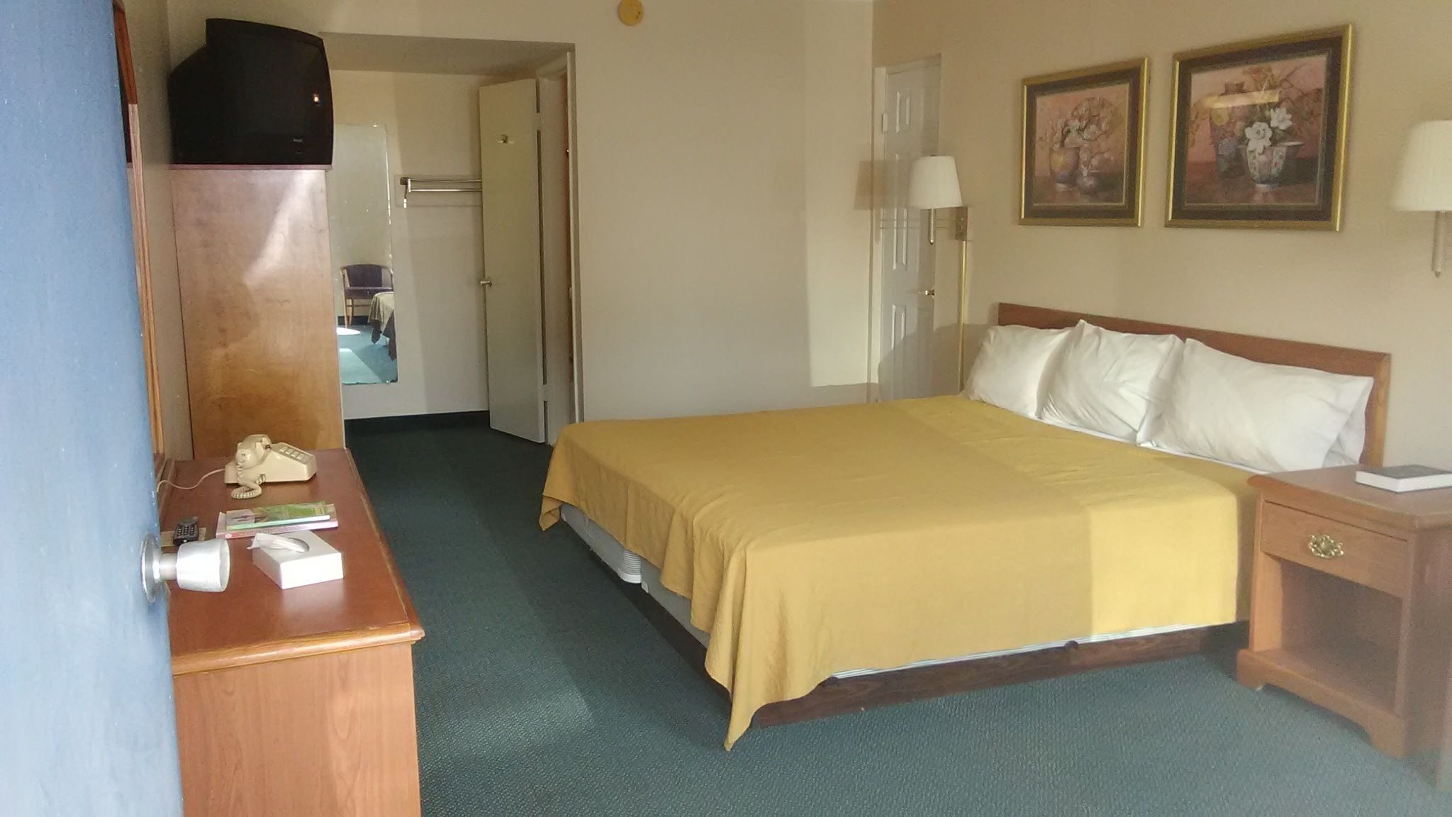 Ein Hotelzimmer mit Bett, Nachttischen, Schreibtisch, Telefon und zwei Bildern an der Wand.