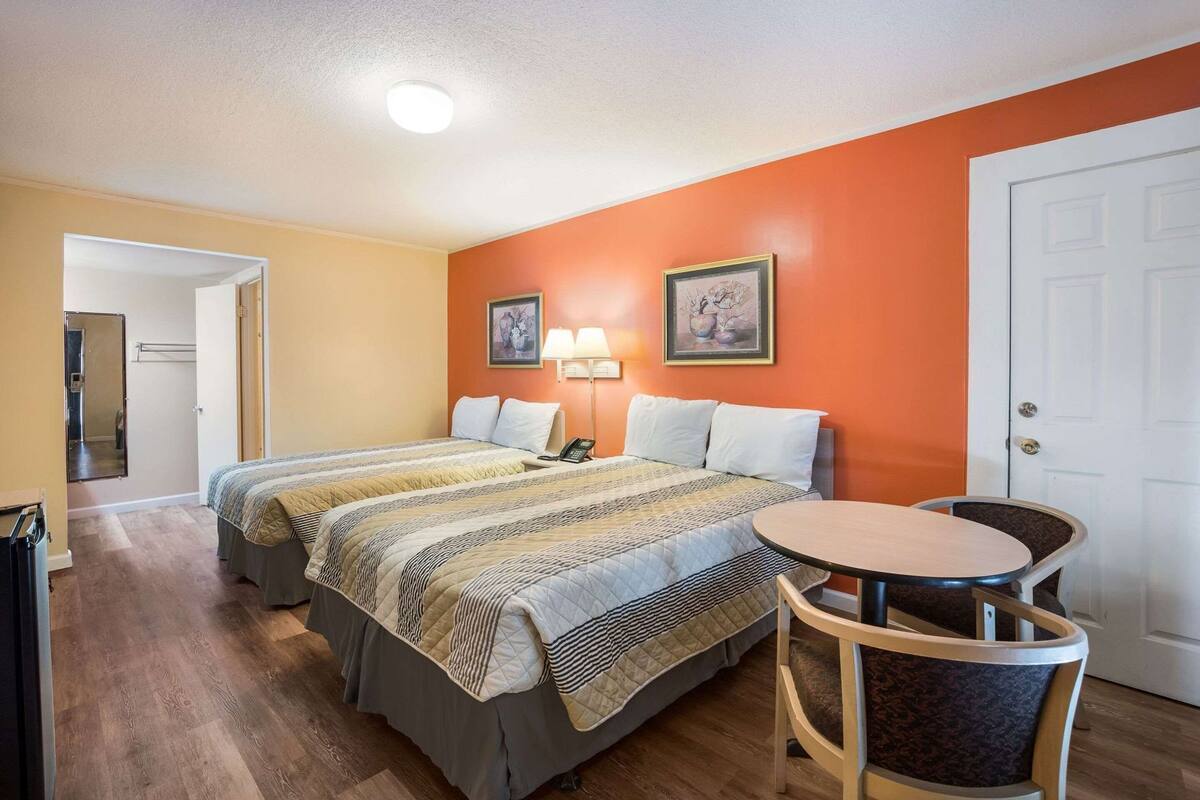 A hotel room with two beds, a round table, a chair, a phone, and two wall-mounted lamps.