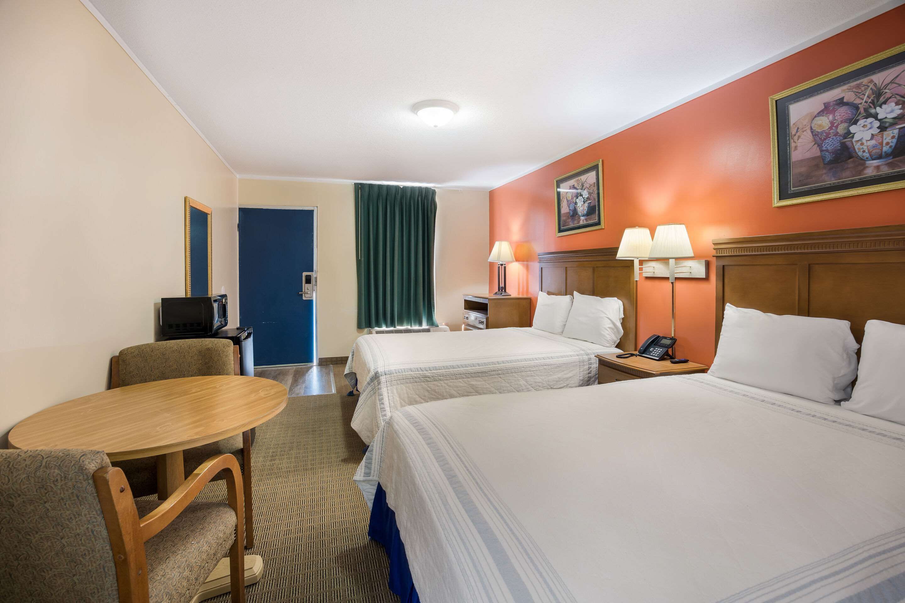 A hotel room with two beds, a desk, a chair, a telephone, and a painting on the wall.