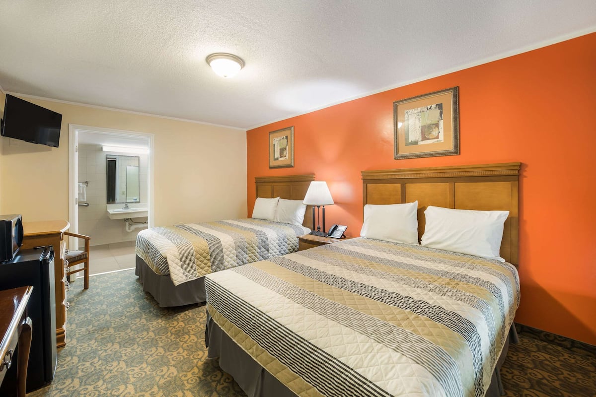A hotel room with two beds, a desk, a chair, a television, and a bathroom visible through an open door.