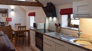 Cucina compatta con forno a incasso, microonde e lavello. C'è un'area pranzo con tavolo e sedie, e una finestra con tende rosse.