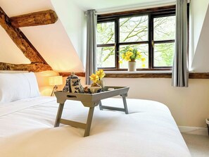 Een slaapkamer met een bed, een raam met gordijnen, een dienblad met een theepot en bloemen, en een lamp.