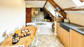 A cozy kitchen with a wooden table, white chairs, a coffee maker, and a stone wall in the background. - 1 bedroom accommodation in Newbridge-on-Wye, near Builth Wells (Newbridge-on-Wye, near Builth Wells)