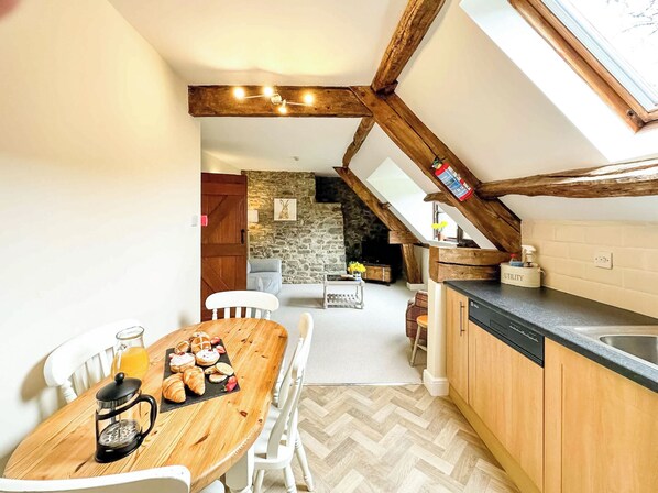 Een gezellige keuken met een houten tafel, witte stoelen, een koffiezetapparaat en een stenen muur op de achtergrond.