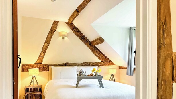 A bedroom with a high ceiling, exposed wooden beams, a bed with white linens, a bedside table with a lamp, and a window with curtains. - 1 bedroom accommodation in Newbridge-on-Wye, near Builth Wells (Newbridge-on-Wye, near Builth Wells)