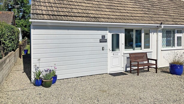 Ein einstöckiges Gebäude mit Ziegeldach, weißer Fassade und einer kleinen Veranda mit einer Bank.