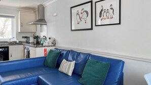 Ein modernes Wohnzimmer mit einem blauen Ecksofa, grün-weiß gestreiften Kissen und gerahmten Bildern an der Wand.