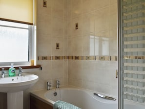 A bathroom with a sink, two faucets, a bathtub, and a window.