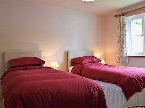 Dos camas con ropa de cama roja, una ventana con cortinas florales y una lámpara a cada lado.
