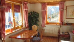 A cozy room with a wooden table and chairs, a large plant, and a view of the outdoors through the windows. - Familiy friendly holiday apartement in a ski area (Sirnitz)