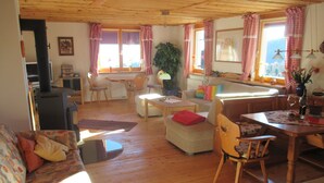 A cozy living room with a sofa, ottoman, and chairs, wooden floors, and large windows with checkered curtains. - Familiy friendly holiday apartement in a ski area (Sirnitz)