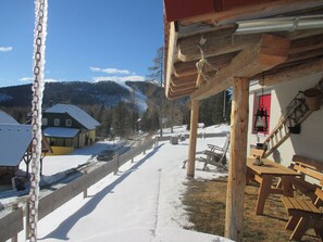 Un edificio de madera con un porche cubierto, un sendero cubierto de nieve y una montaña al fondo.