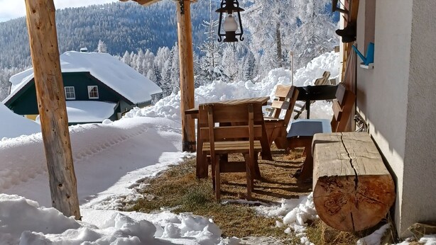A wooden cabin with a covered porch, a table, and chairs. - Familiy friendly holiday apartement in a ski area (Sirnitz)
