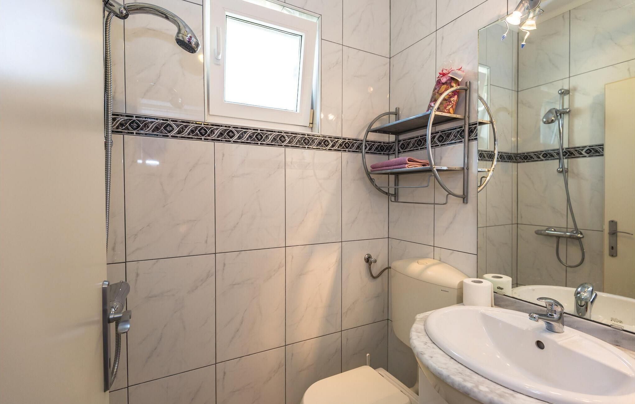 Une salle de bain équipée d’un WC, d’un lavabo et d’une douche. On y trouve un porte-serviettes avec une serviette et une boîte cadeau.