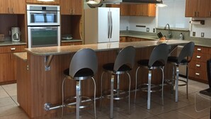 A modern kitchen with wooden cabinets, stainless steel appliances, and a central island with bar stools. - On Open Gulf, luxury home on safe private road, large dock/deck, gourmet kitchen (Cedar Key)