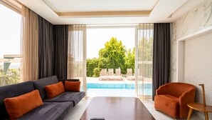 Una sala de estar moderna con un sofá, una mesa de centro y una silla, con vista a una piscina y jardines.
