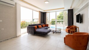Una sala de estar moderna con un sofá seccional gris, sillones naranja y un televisor de pantalla plana montado en la pared.
