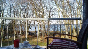 Ein Balkon mit Tee-Gedeck, Blick auf Wald und Gewässer.