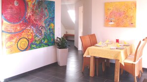 Ein Essbereich mit einem Tisch für vier Personen, Holzkästen und zwei große abstrakte Gemälde an den Wänden.