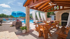 Un espace extérieur aménagé en bois, avec une table à manger, une piscine et des chaises longues en arrière-plan.